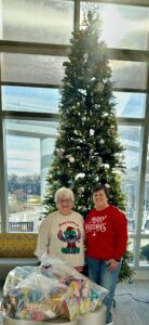 Peggy Sohl and Jeanine Spencer with bags of gifts in front of the Stony Brook Children's Hospital Christmas tree
