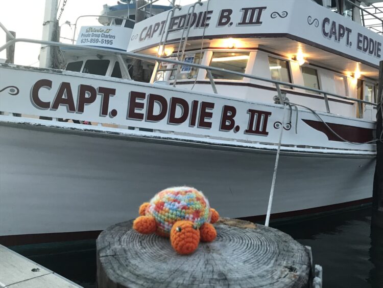 Toy turtle on a dock piling in front of the Captain Eddie B III charter fishing boat
