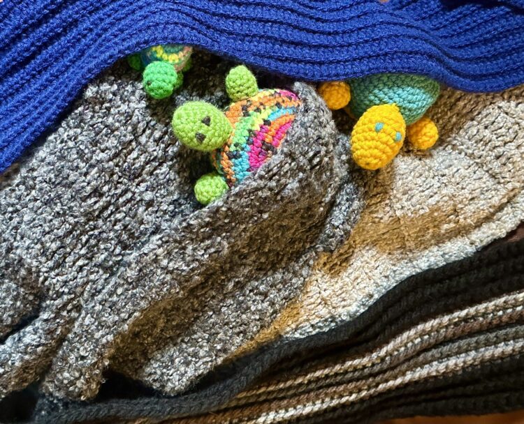 Three toy turtles peering out from beneath hand-crocheted blankets