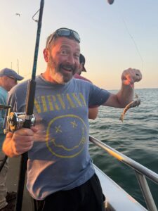 A smiling man holding a fishing pole with a bait fish on the hook